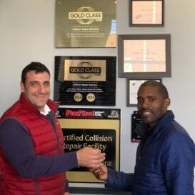 Two men shaking hands in front of a wall with awards and certificates. Two men shaking hands in front of a wall with awards and certificates.